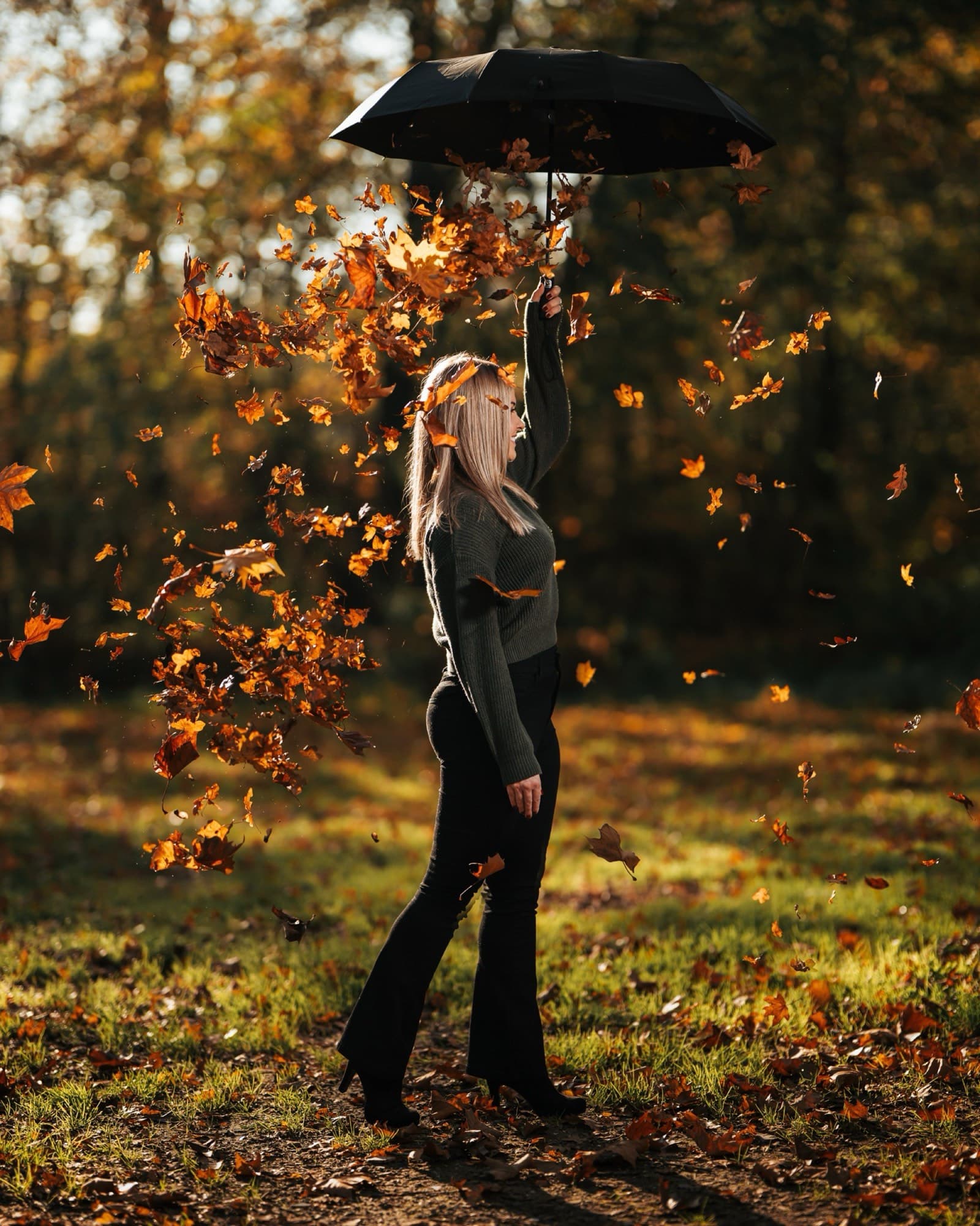 Vrouw met paraplu tussen dwarrelende herfstbladeren, warm tegenlicht